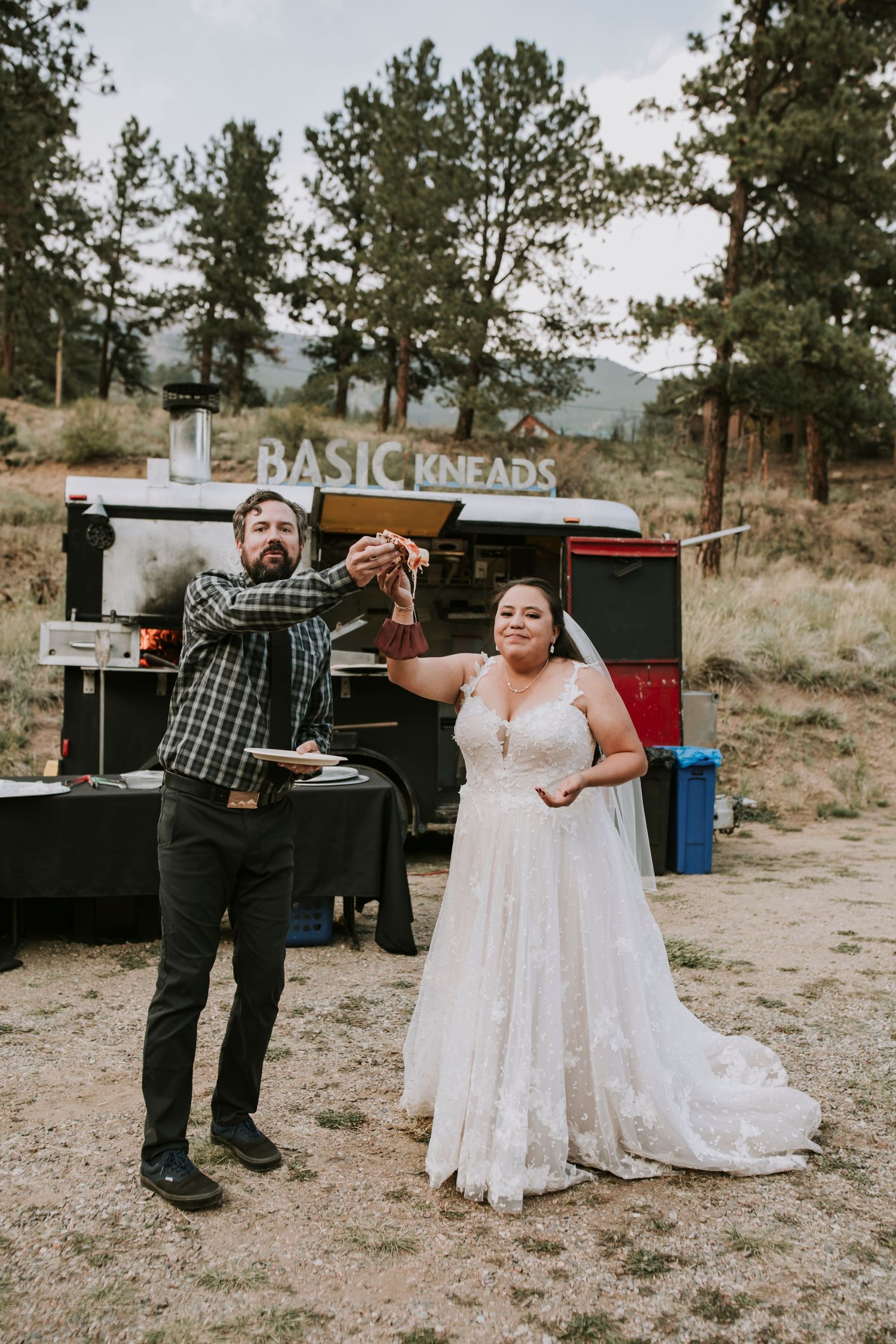 Bride and groom holding up pizza slices in front of wood fired pizza truck