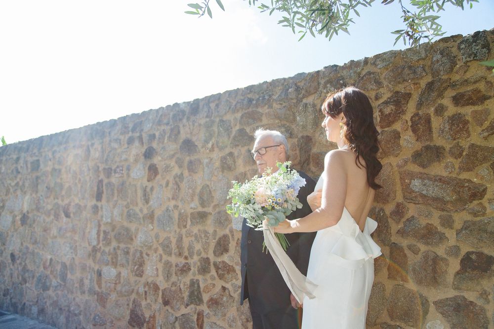 Wedding ceremony moment against rustic stone wall backdrop in natural sunlight.