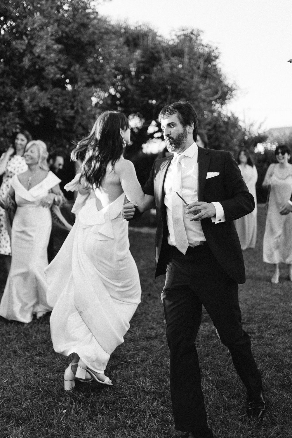 A couple dances energetically on a lawn during a formal outdoor event.