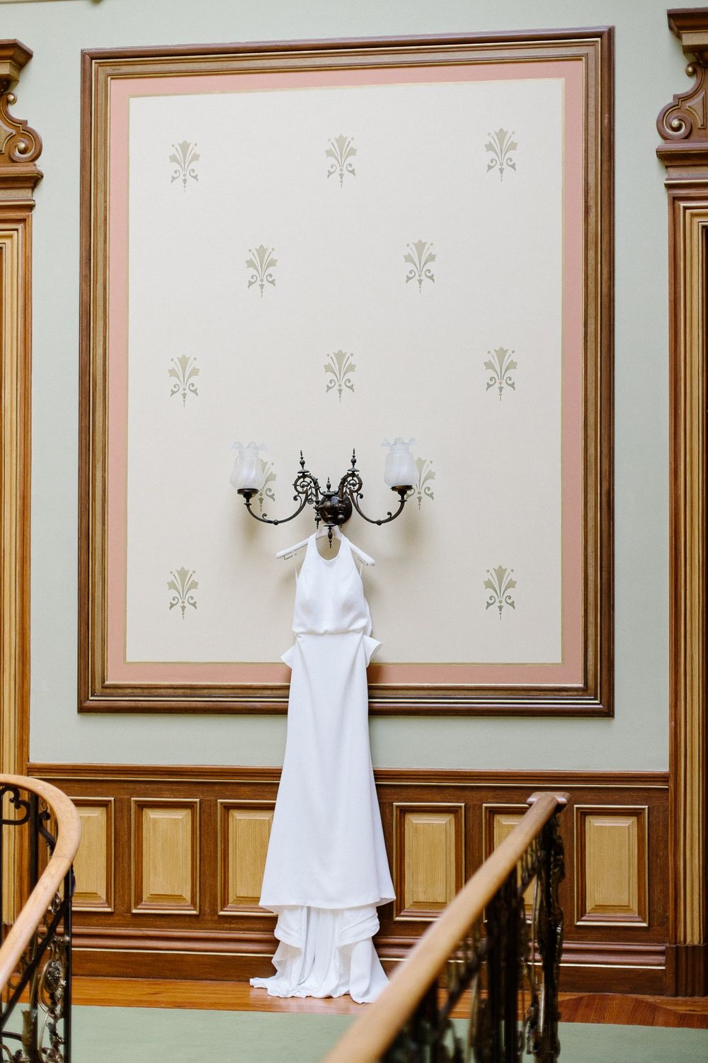 White wedding dress hanging on ornate wall sconce against decorative wallpaper.