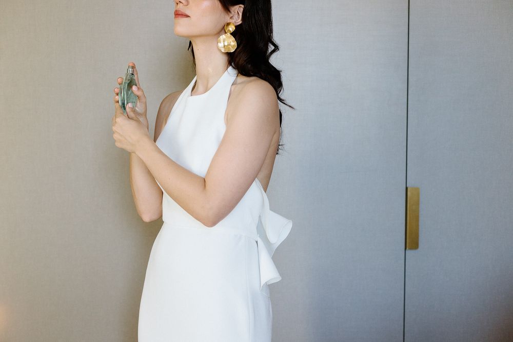 Side profile of someone in an elegant white dress holding a perfume bottle.