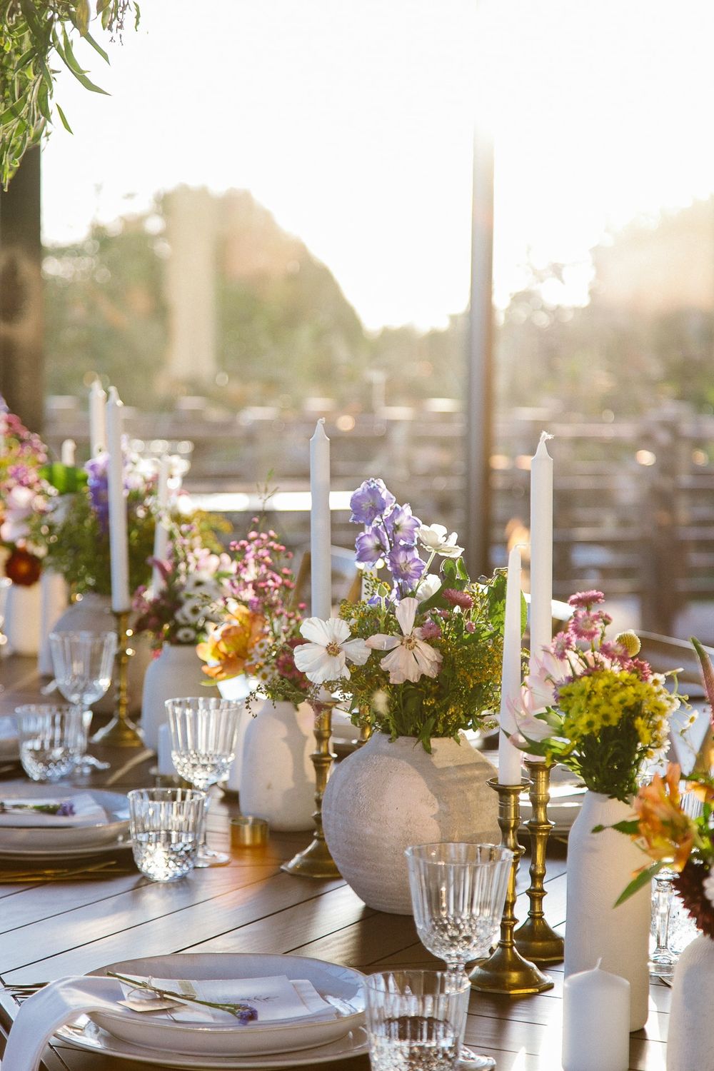 Sunlit wedding table with floral centerpieces, candles, and elegant place settings.