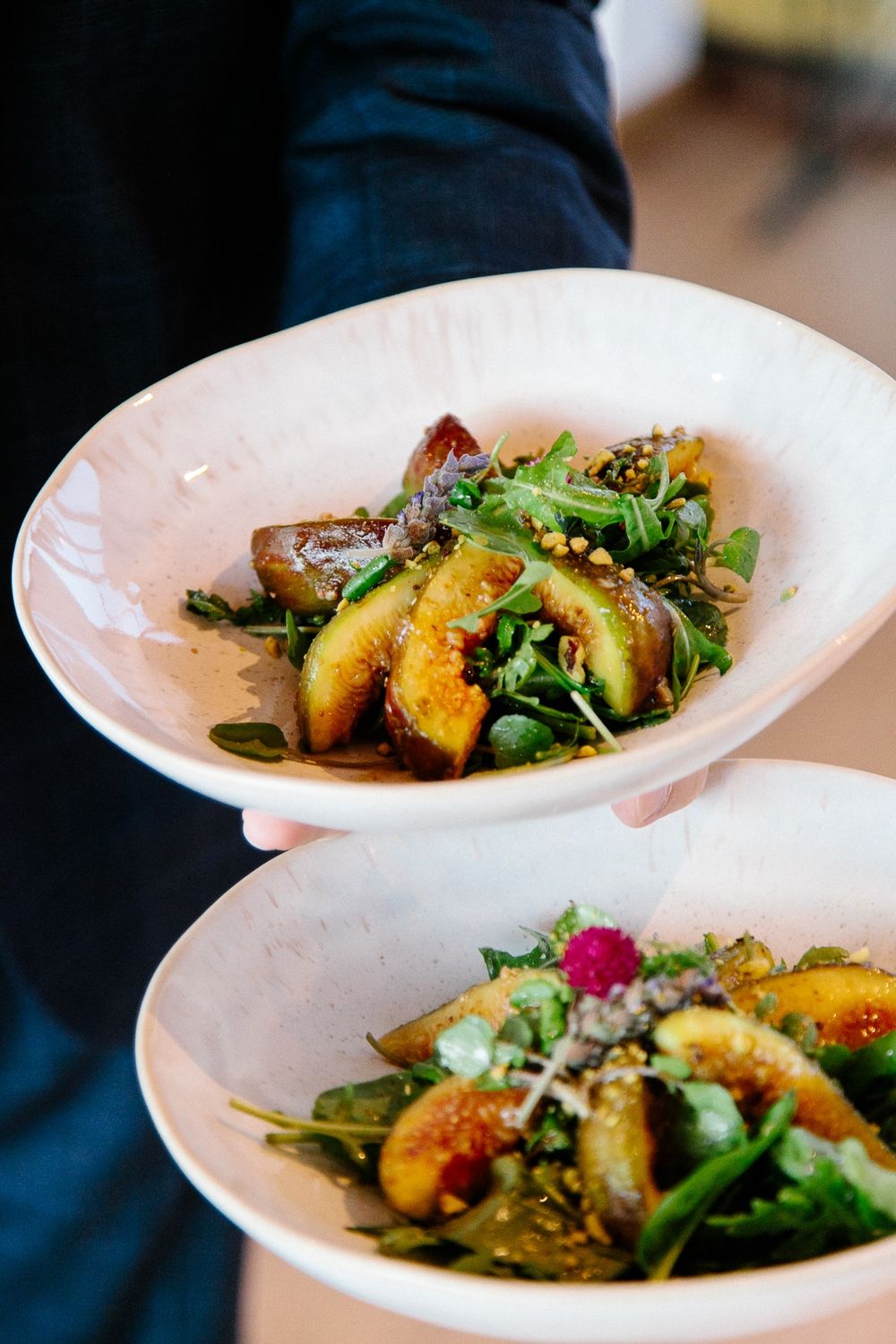 Beautifully plated salad with grilled peaches, greens and edible flowers on white ceramic dishes.