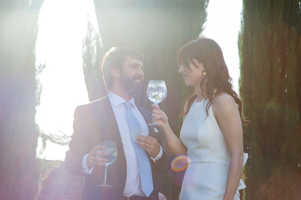 Elegant couple sharing wine glasses during sunset at an outdoor celebration.