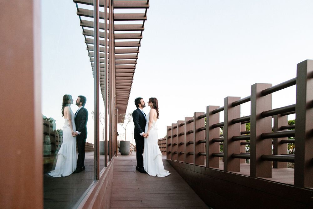 Architectural wedding photo showing reflection in modern wooden pergola structure.