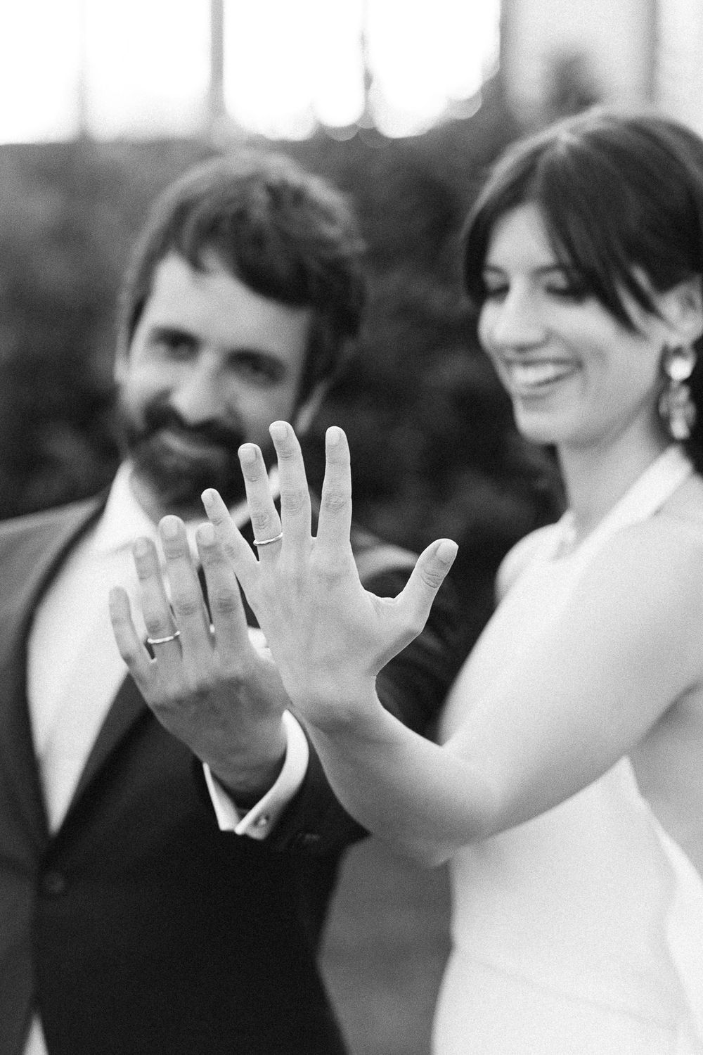 A black and white photo of newlyweds showing off their wedding rings.