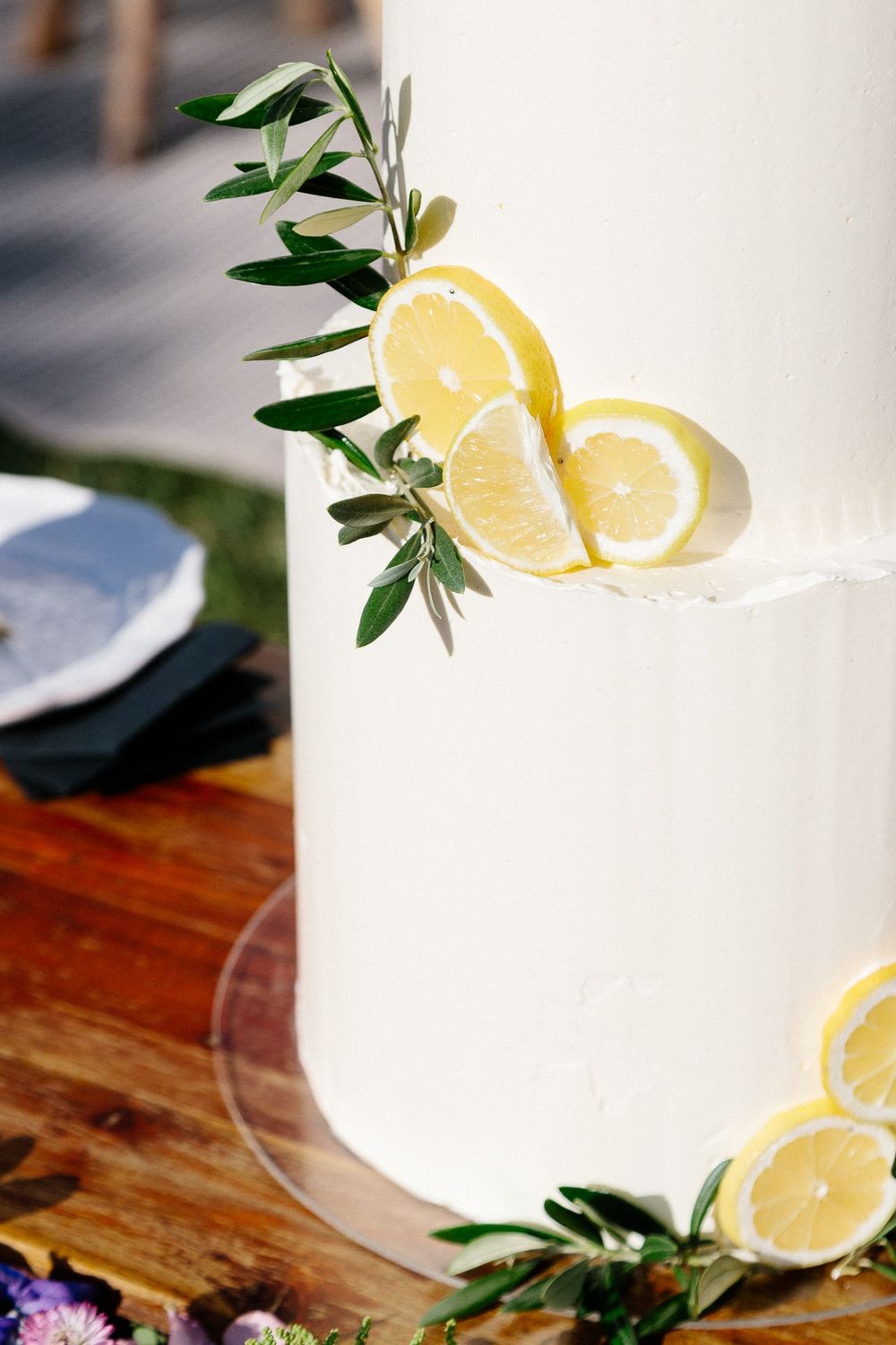 Fresh lemon slices and greenery decorating a white wedding cake on a wooden table.