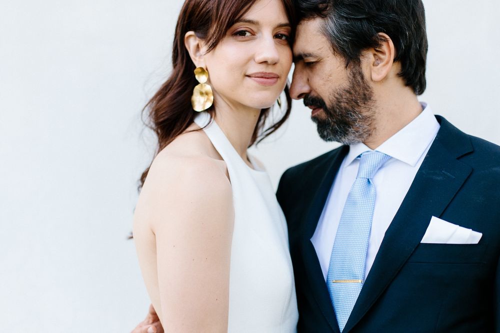 A romantic close-up portrait of a couple in wedding attire against a white wall.