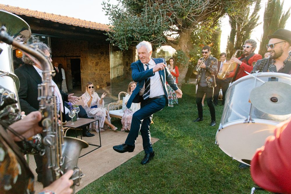 Guests dance joyfully at an outdoor wedding reception as others play musical instruments on a patio.