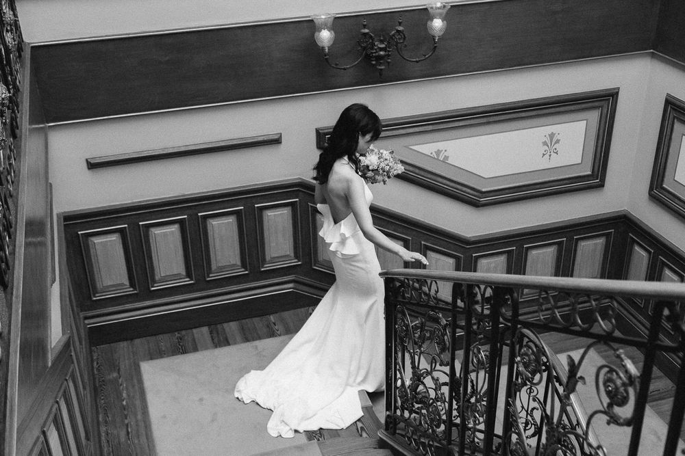 Dramatic black and white staircase shot of flowing wedding gown with architectural details.