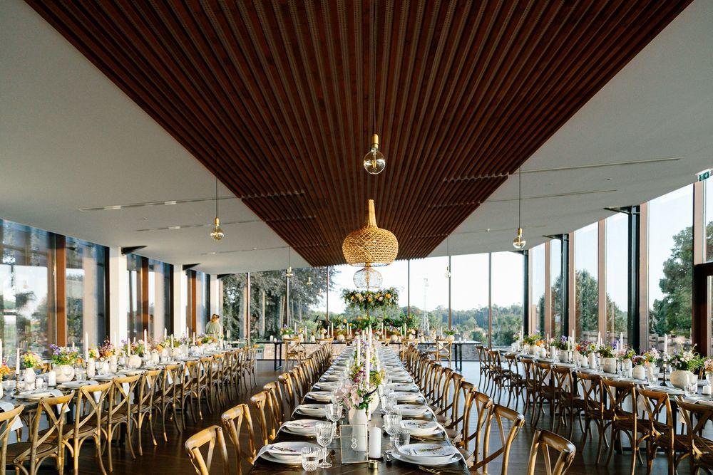 Modern wedding reception venue with wooden slat ceiling and floor-to-ceiling windows overlooking nature.
