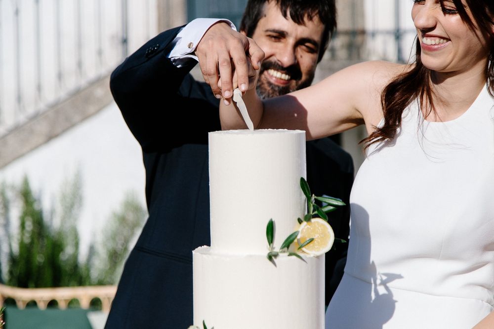 A couple cutting their elegant white wedding cake together outdoors.