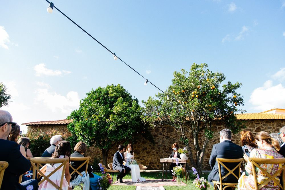 An outdoor wedding ceremony setup with wooden chairs against a stone wall under blue skies.