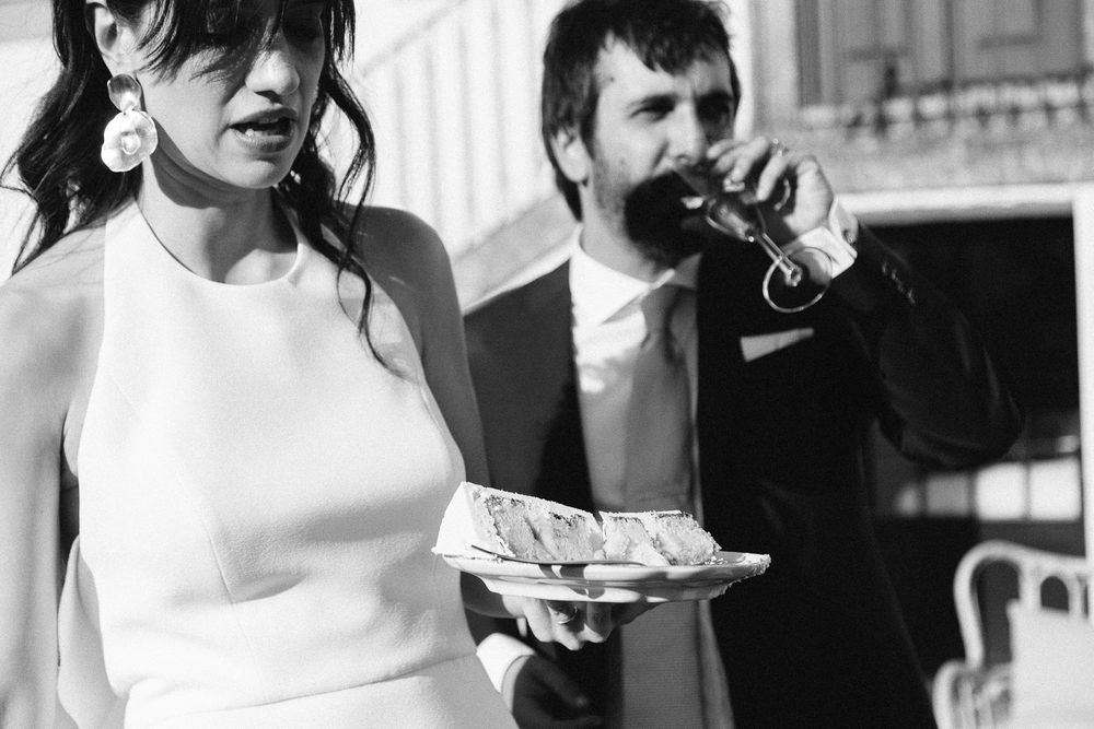 A black and white wedding photo capturing a couple enjoying cake and drinks at their reception.