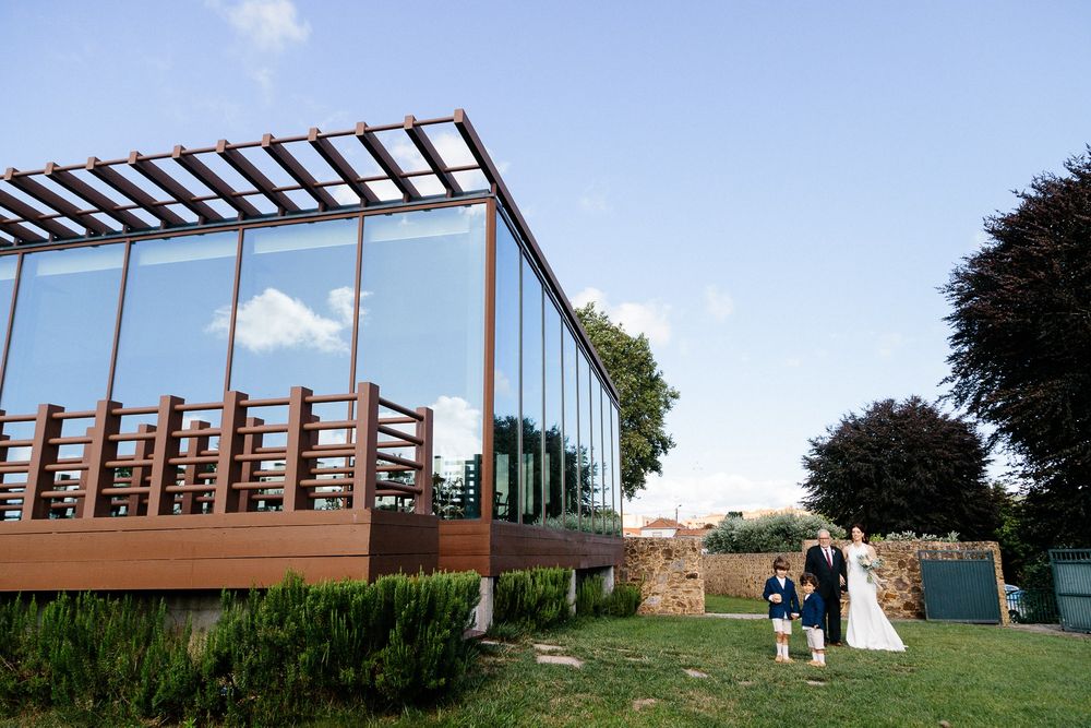 Modern glass wedding venue with wooden pergola structure against blue sky.