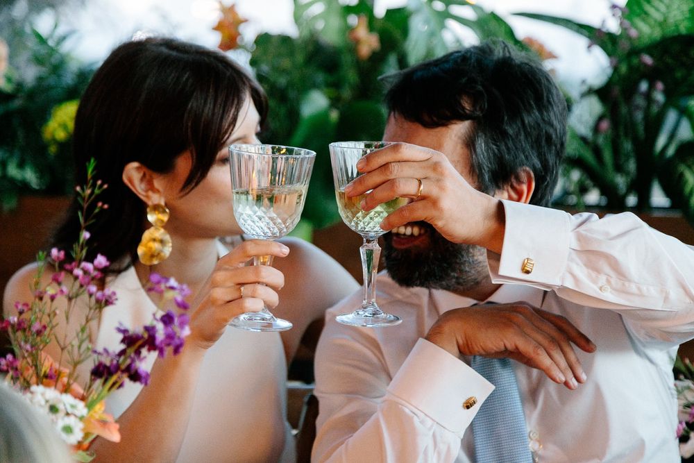 Playful toast moment between couple with floral decor and crystal glasses.