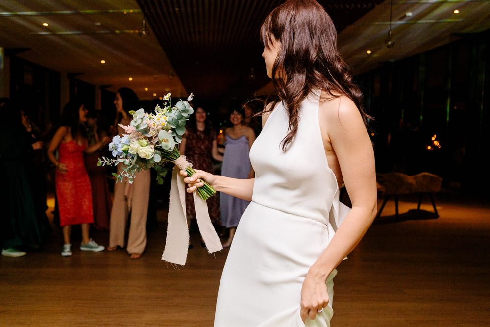 A wedding bouquet is held by a bride in a white dress at an indoor reception venue.
