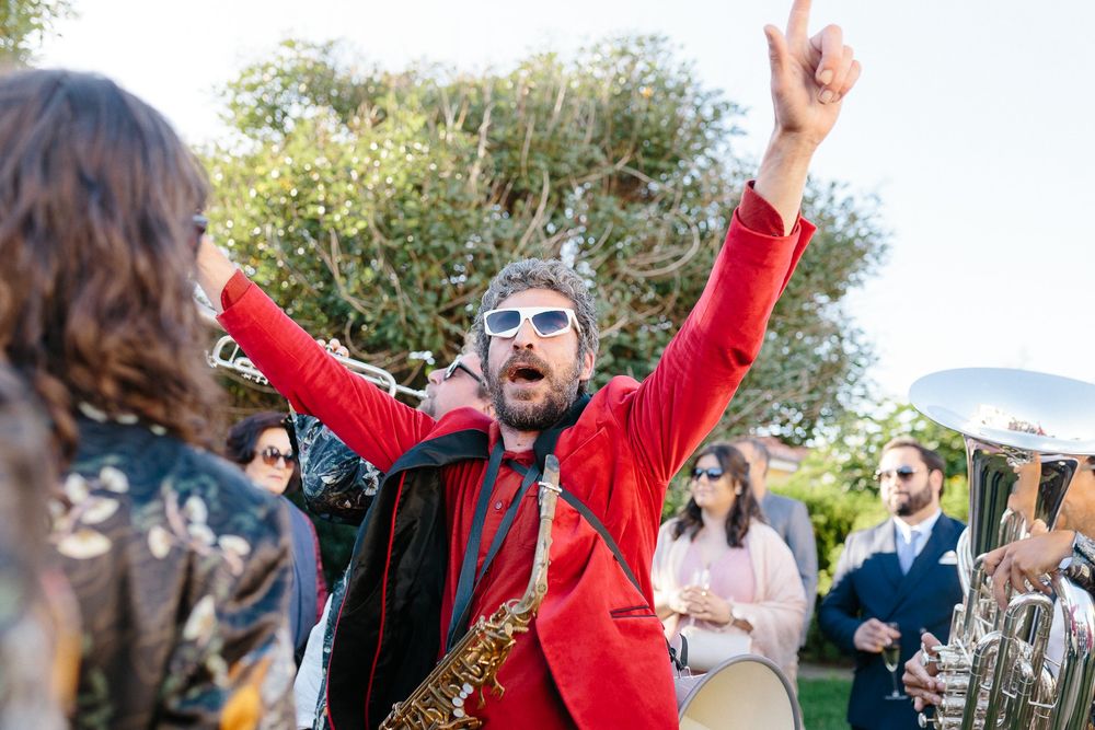 A musician in a red jacket performs energetically at an outdoor wedding celebration.