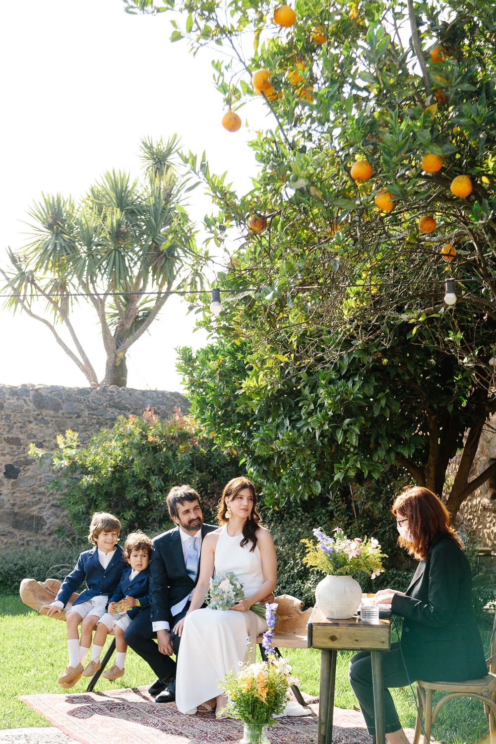 A citrus tree laden with oranges frames an intimate outdoor wedding ceremony.