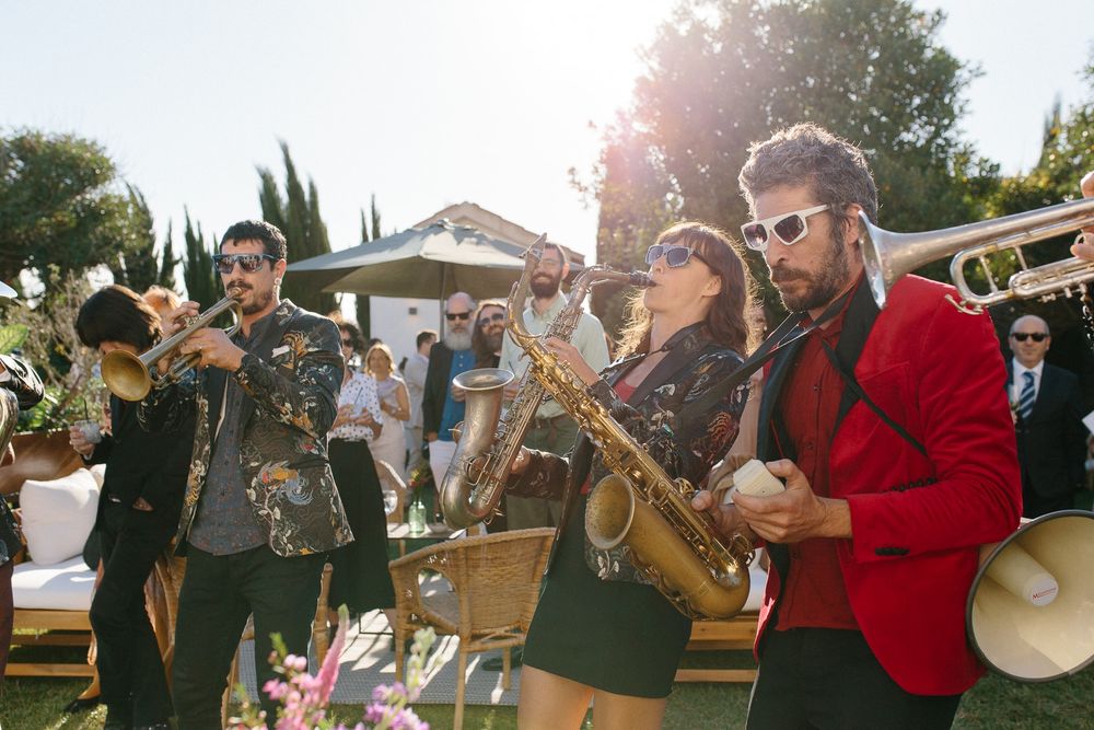 A lively brass band in casual attire performs at an outdoor wedding celebration.