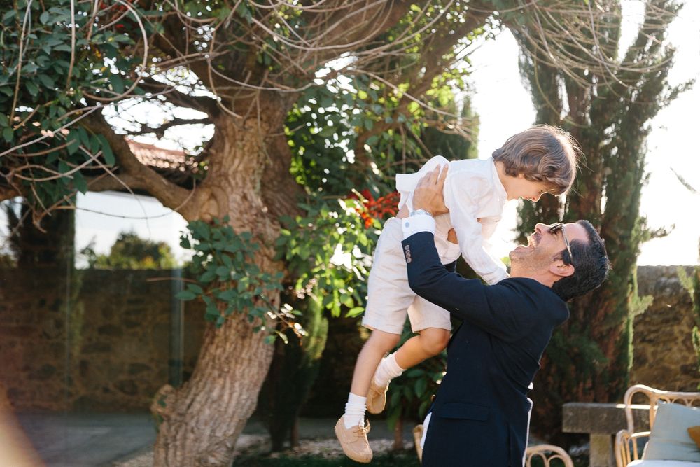 A tender outdoor moment shared between two figures against a sunlit garden backdrop with trees.