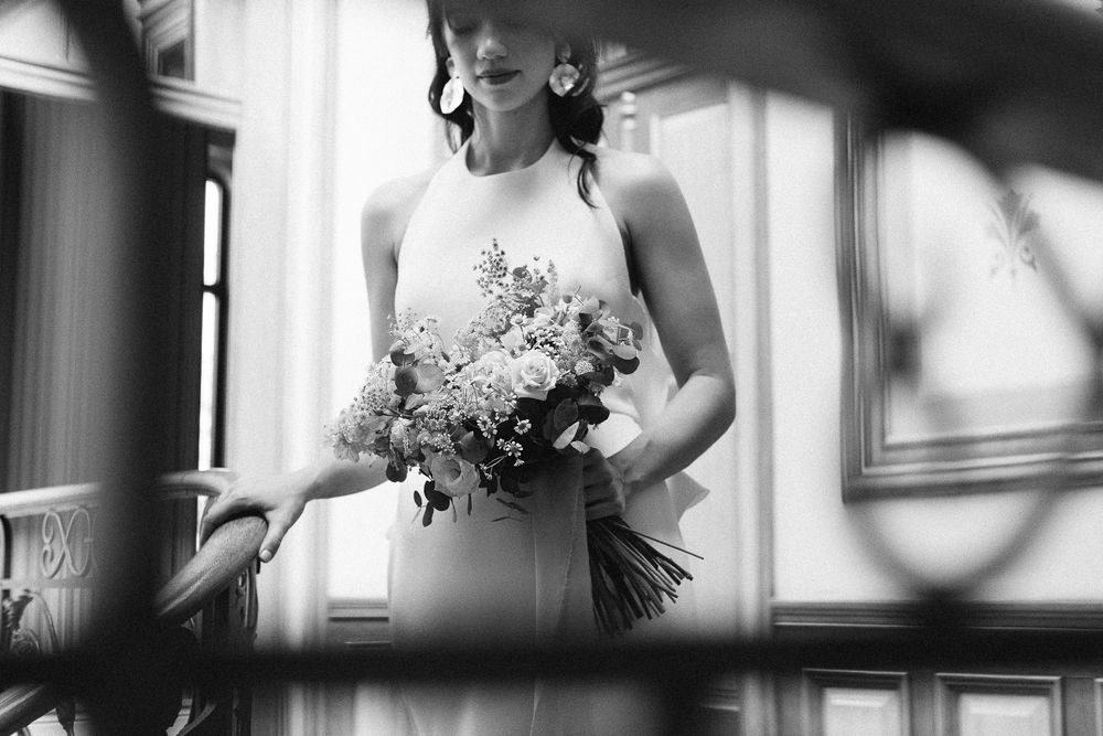 Elegant bridal portrait in black and white showing delicate lace details and wedding bouquet through ornate railings.