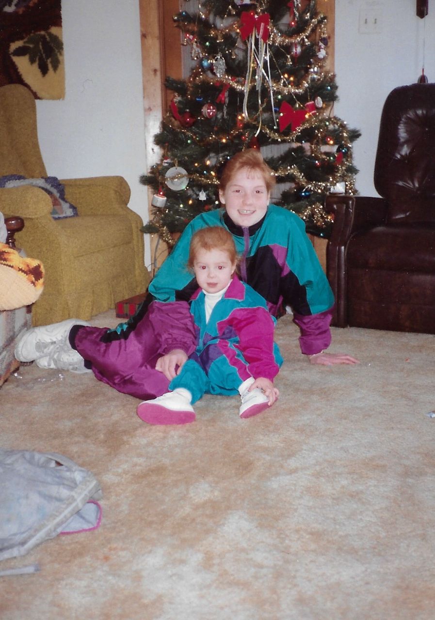 A holiday scene with two people in matching teal and purple outfits sitting by a decorated Christmas tree.