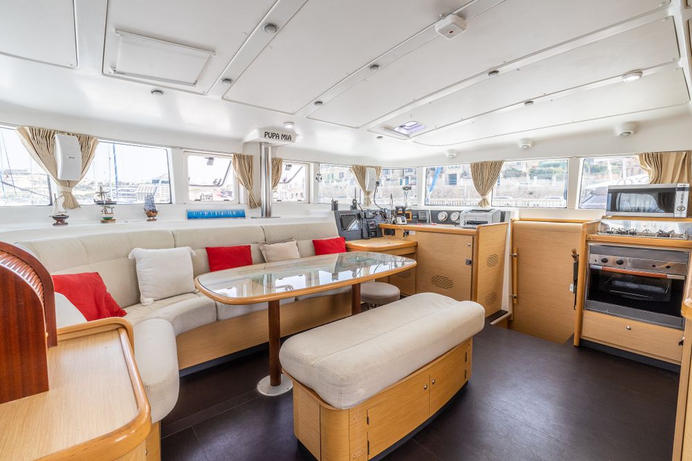 Luxury catamaran interior salon with white cushioned seating, wooden cabinetry, and red accent pillows.