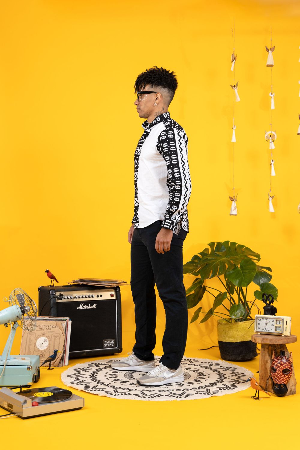 Stylish young man in patterned black white jacket posing in vibrant yellow studio with vintage decor.