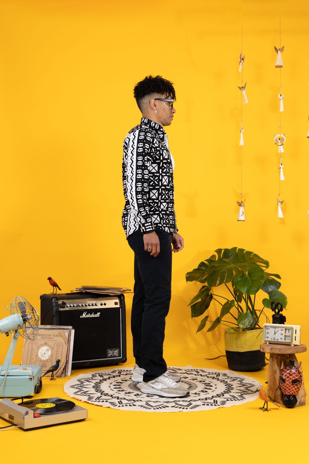 Young man in black white patterned jacket standing in yellow studio with retro music props.