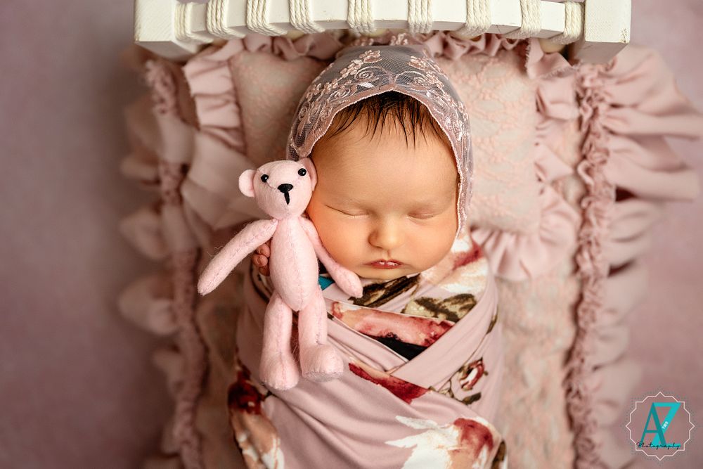 Sleeping newborn with pink teddy bear in delicate pink setting during professional photo session.