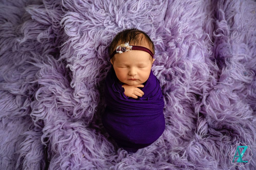 Sleeping newborn wrapped in purple fabric on matching textured fur backdrop.