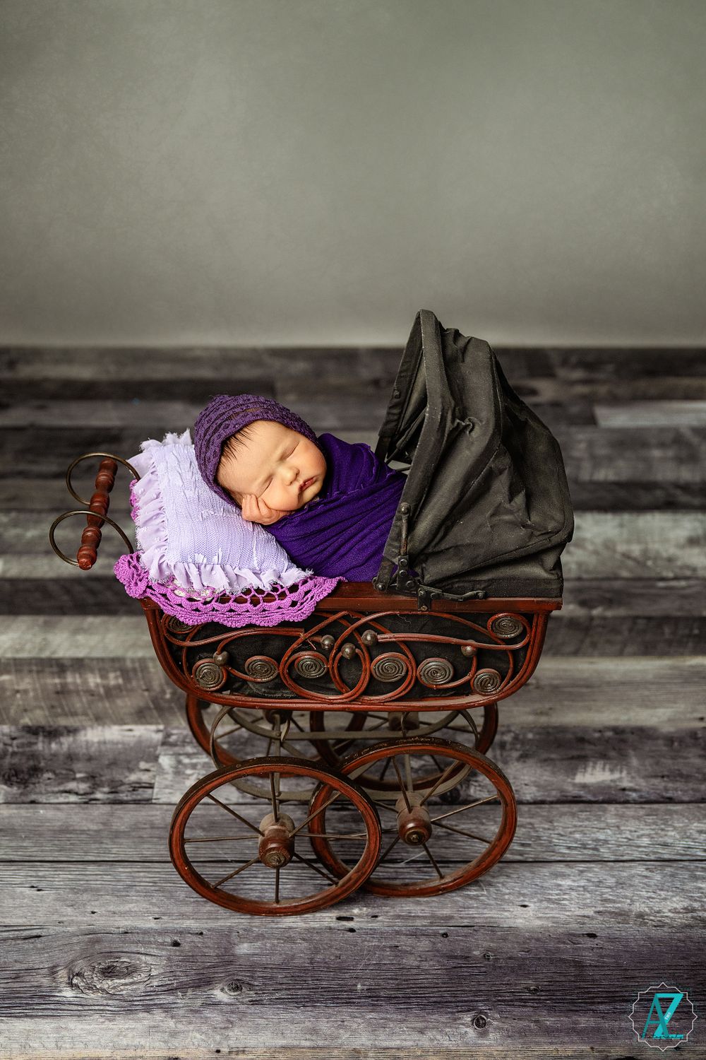 Vintage baby carriage with purple and pink accents on rustic wooden floor in black and white photo.