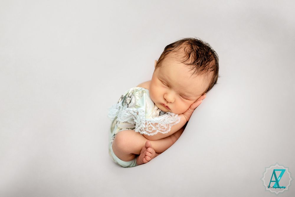 Serene newborn portrait in mint green wrap against white background during studio session.
