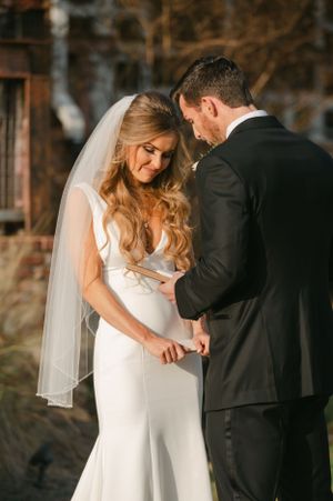 Bride and groom holding hands in tender first look moment, bride wearing elegant white gown with veil outdoors.