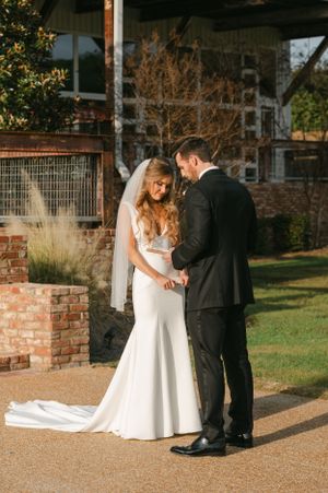 Bride and groom share a tender moment holding hands outside a rustic brick venue on their wedding day.