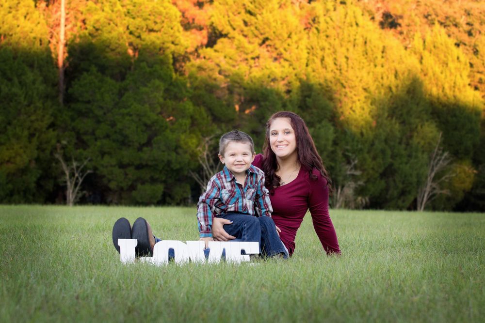 Mother holding her son sitting on the ground next to a sign that says love at sunset.