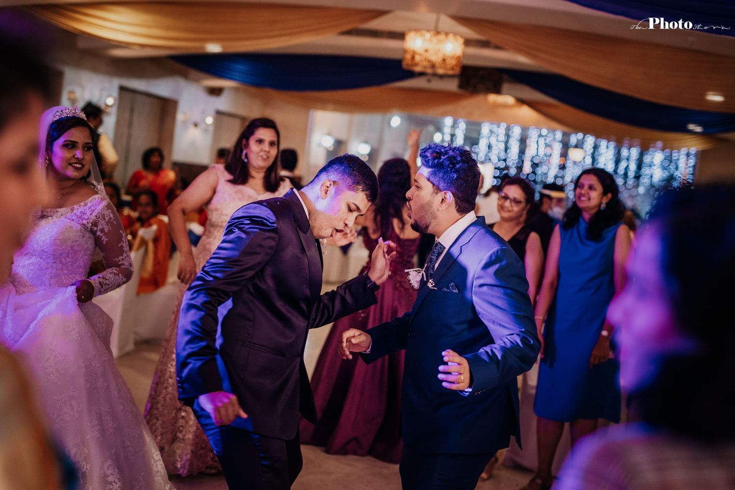 Wedding guests dancing and celebrating under warm ambient lighting at reception.