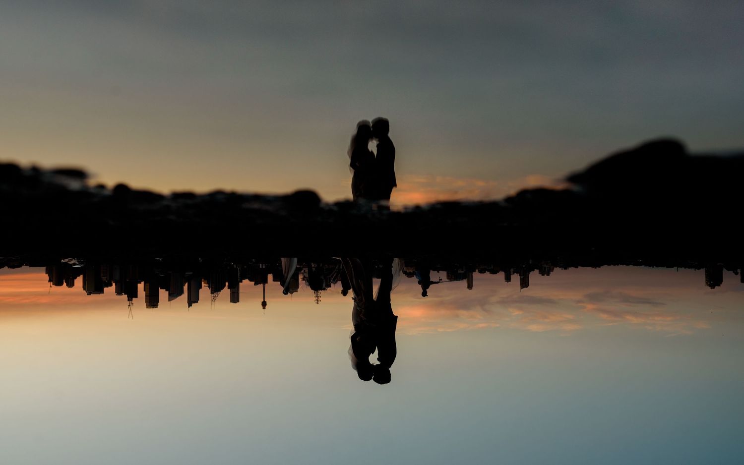 Romantic couple silhouette reflected in still water at sunset.