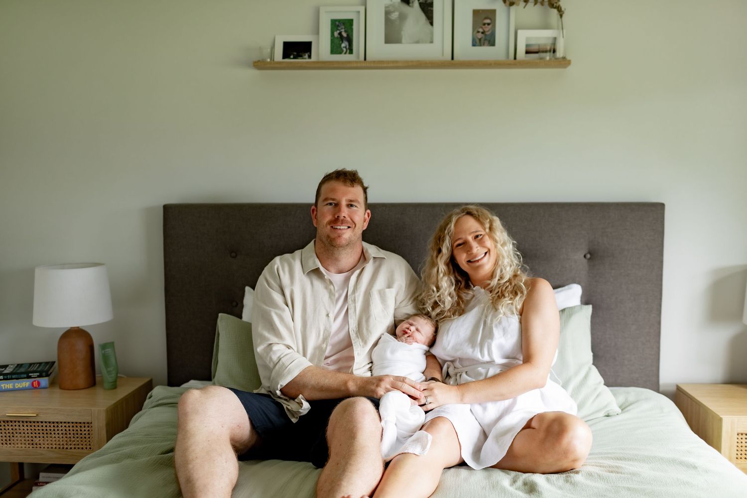 Intimate family moment on a bed with gray upholstered headboard and white bedding.