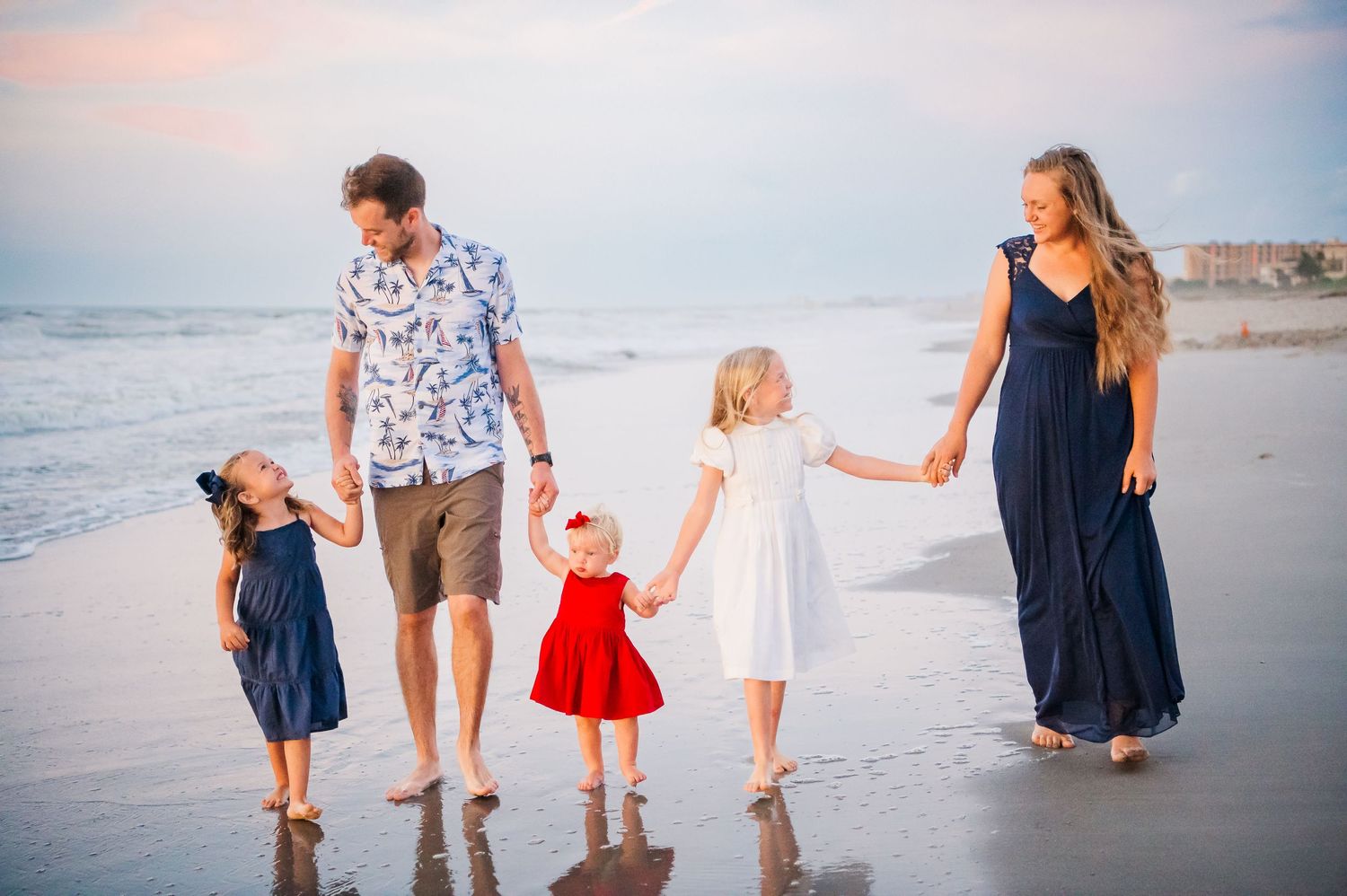 A family of four walking hand in hand along the beach at sunset.