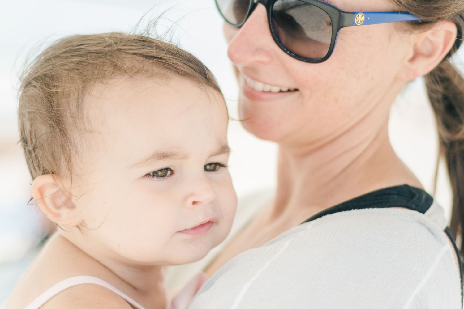 Parent in sunglasses holding small child against bright background.