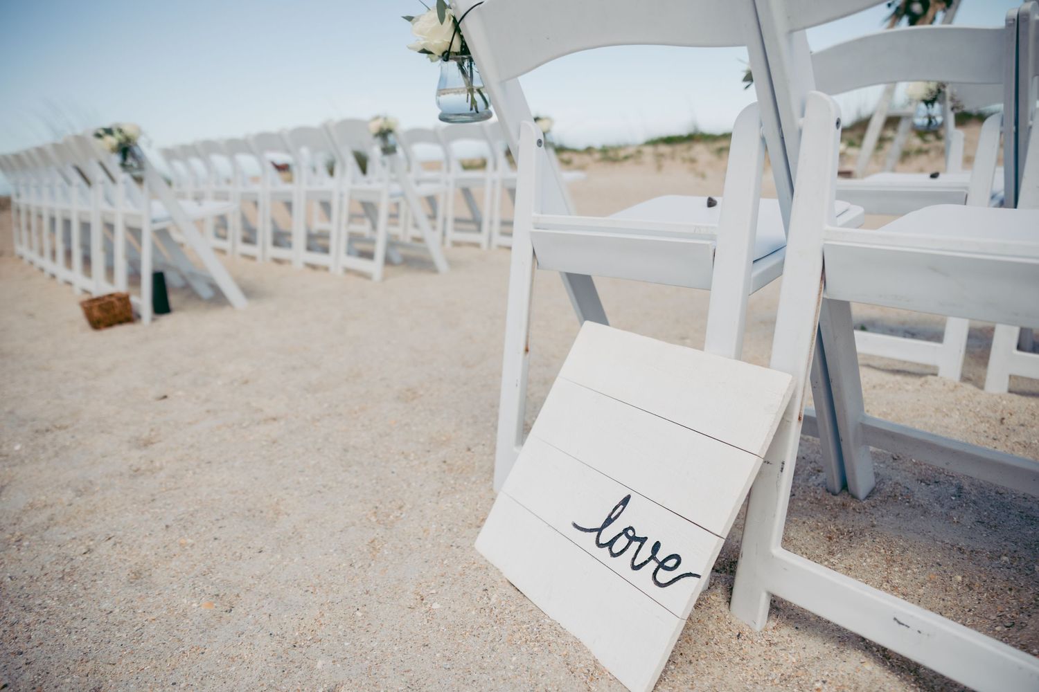 White wooden chairs arranged in rows on a beach with love sign decoration.
