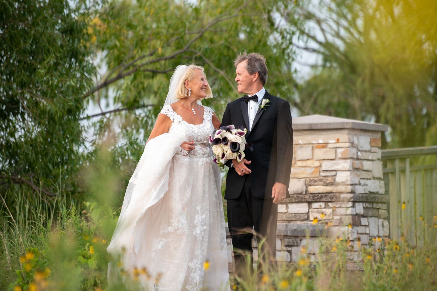 Elegant wedding couple shares a romantic moment in front of stone pillars at sunset.
