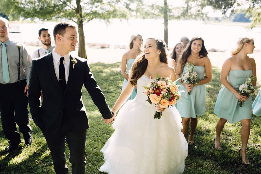 Wedding party laughs together outdoors in formal attire with bridesmaids in mint green dresses.