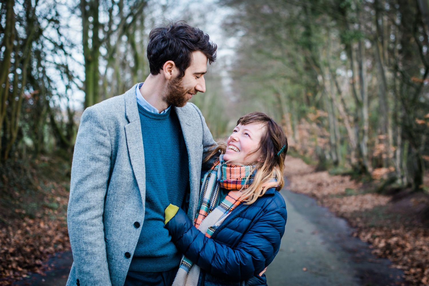 couple wrapped up warm their winter shoot, smiling and laughing at each other.