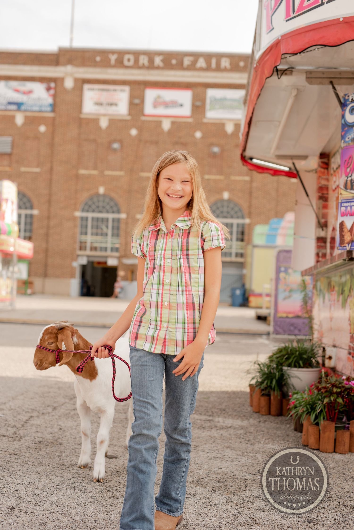 A handler with a goat poses in front of the historic York Fair building.