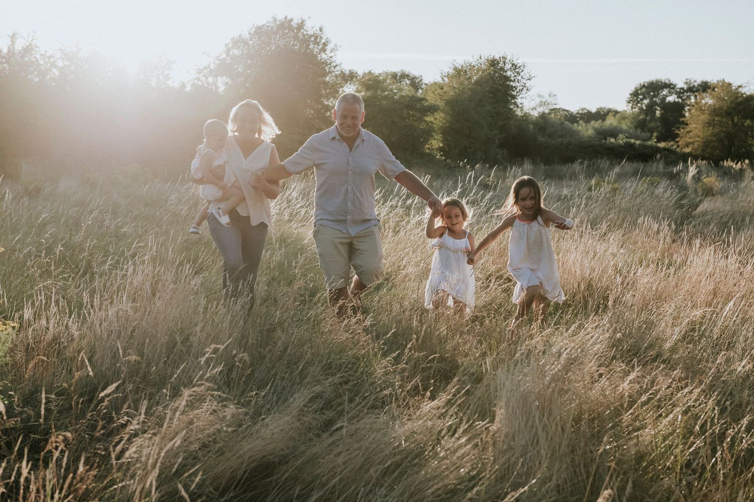 Family holding hands while walking through tall grass at sunset.