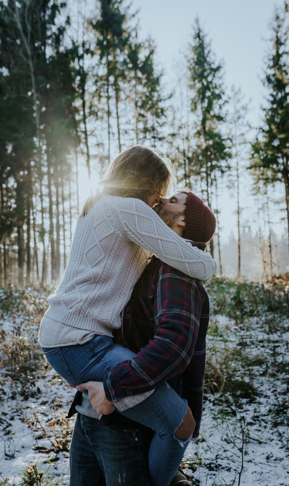 Couple in winter clothing sharing romantic moment in snowy forest landscape.