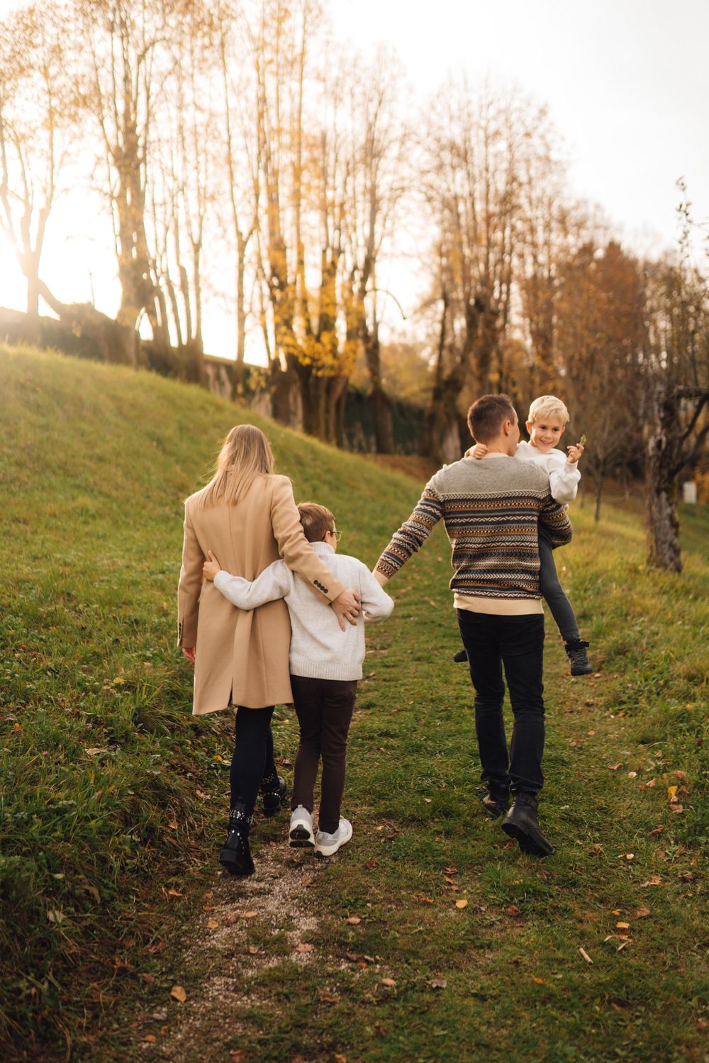 A family walking together up a grassy hill during autumn with trees in the background.